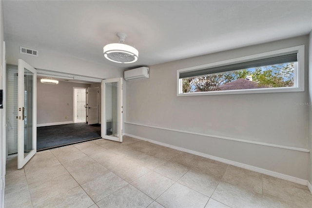 spare room featuring french doors, a wall unit AC, and light tile patterned flooring