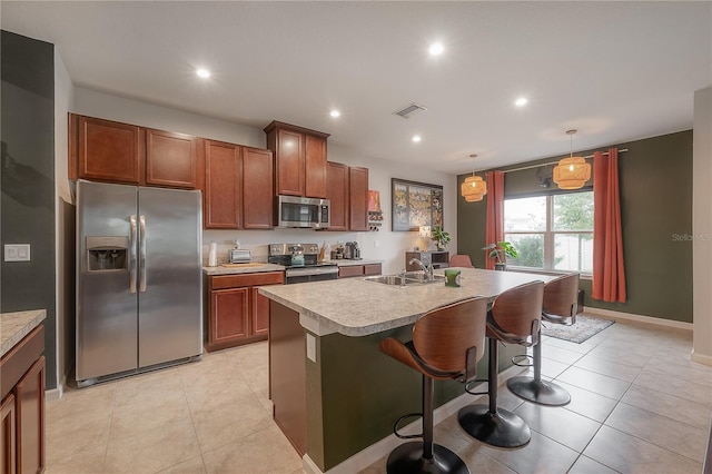 kitchen with sink, hanging light fixtures, a kitchen breakfast bar, a kitchen island with sink, and appliances with stainless steel finishes