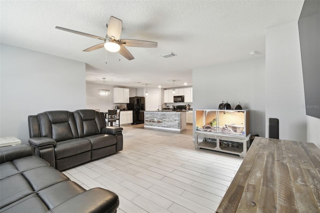 living room with a textured ceiling, light hardwood / wood-style flooring, ceiling fan, and sink