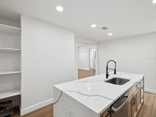 kitchen with sink, stainless steel dishwasher, an island with sink, hardwood / wood-style flooring, and light stone countertops