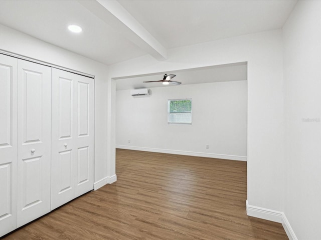 unfurnished bedroom with beamed ceiling, wood-type flooring, a wall mounted AC, ceiling fan, and a closet