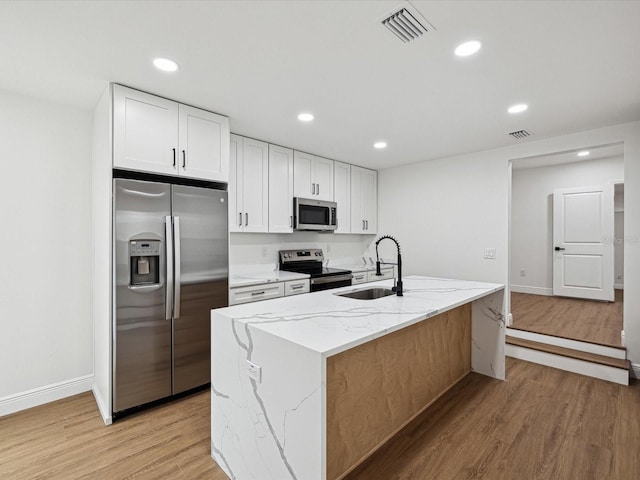 kitchen with white cabinetry, light wood-type flooring, appliances with stainless steel finishes, light stone countertops, and a kitchen island with sink