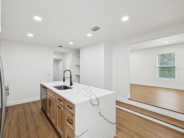 kitchen featuring sink, light wood-type flooring, stainless steel dishwasher, light stone countertops, and a kitchen island with sink