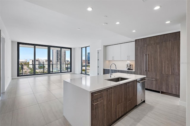 kitchen featuring white cabinetry, sink, expansive windows, stainless steel dishwasher, and a center island with sink