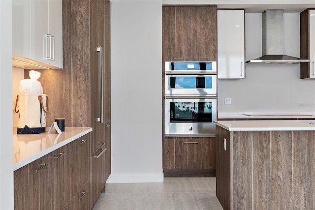 kitchen with white cabinetry, wall chimney exhaust hood, cooktop, double oven, and light tile patterned floors