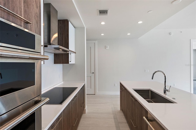 kitchen featuring wall chimney exhaust hood, stainless steel double oven, black electric cooktop, and sink