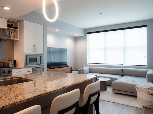 kitchen featuring light stone countertops, a breakfast bar, open floor plan, stainless steel microwave, and white cabinets