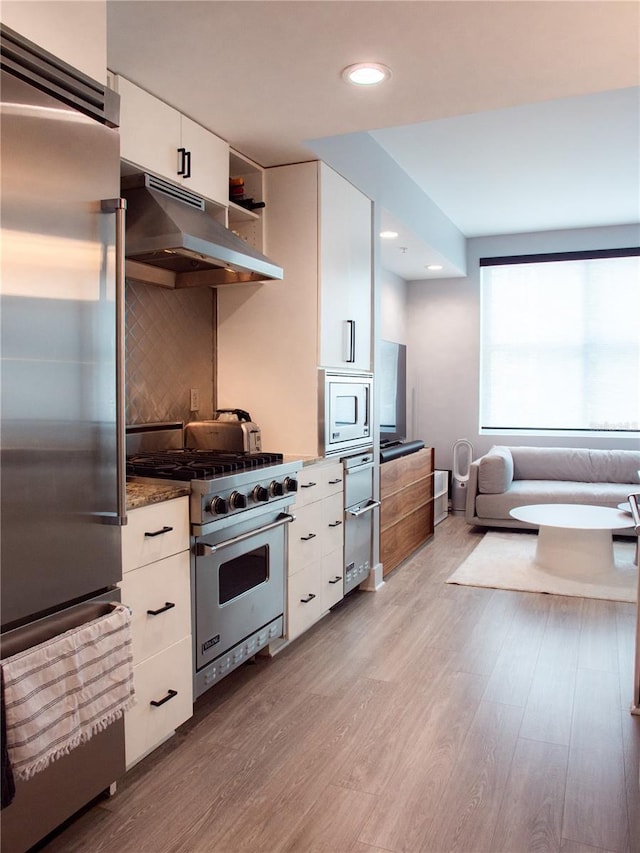 kitchen with light wood-style flooring, white cabinetry, built in appliances, and under cabinet range hood