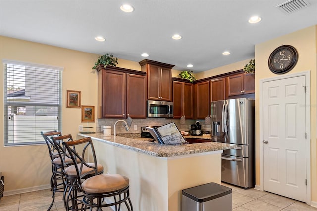 kitchen with a breakfast bar, light tile patterned floors, light stone countertops, appliances with stainless steel finishes, and kitchen peninsula