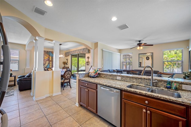 kitchen featuring light stone counters, ornate columns, ceiling fan with notable chandelier, sink, and dishwasher