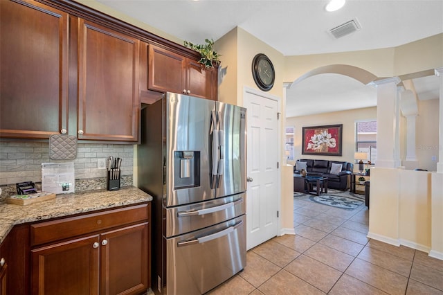 kitchen featuring ornate columns, light stone countertops, stainless steel refrigerator with ice dispenser, backsplash, and light tile patterned flooring