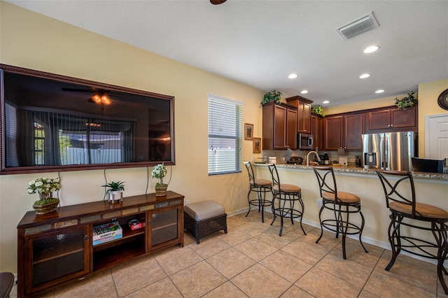 kitchen featuring kitchen peninsula, a kitchen bar, backsplash, stainless steel appliances, and light tile patterned flooring