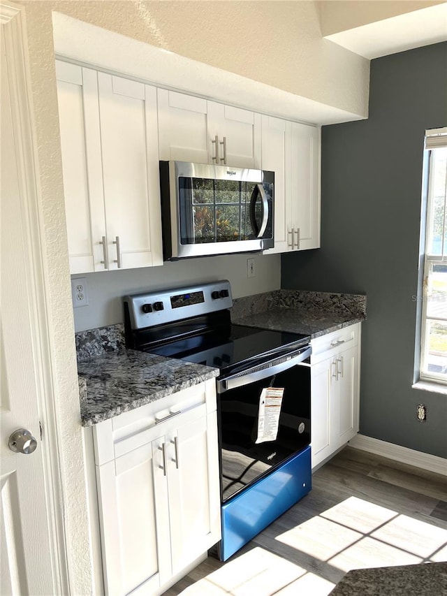 kitchen with white cabinets, light wood-type flooring, stainless steel appliances, and dark stone countertops