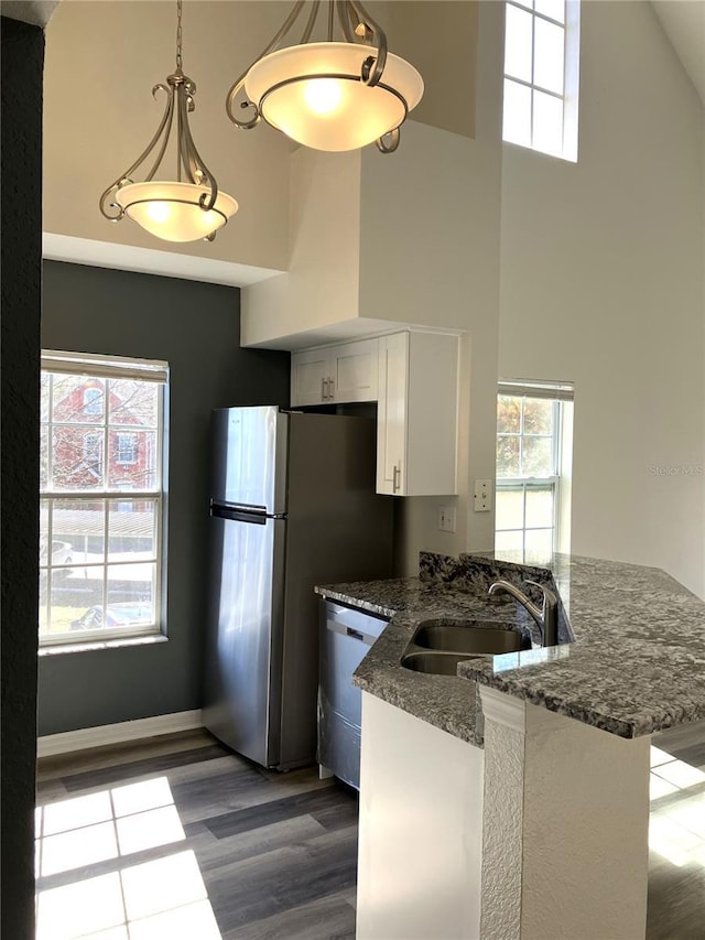 kitchen featuring pendant lighting, high vaulted ceiling, sink, dark stone countertops, and white cabinetry