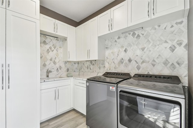 laundry room with sink, washing machine and dryer, cabinets, and light wood-type flooring