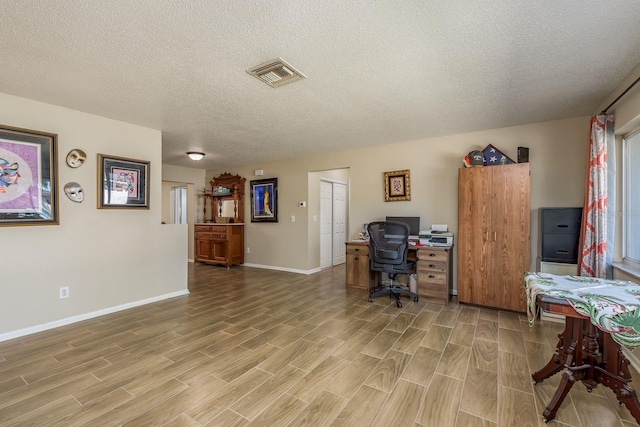 office with visible vents, light wood finished floors, baseboards, and a textured ceiling