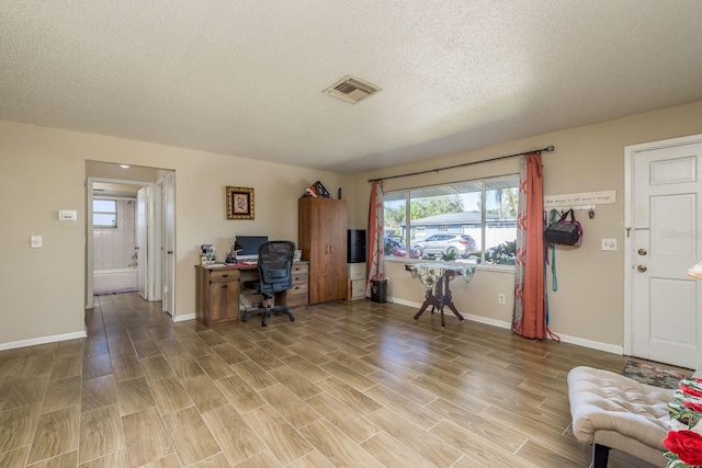 office featuring a textured ceiling, light wood-style flooring, visible vents, and baseboards