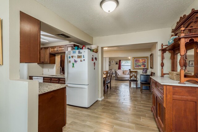 kitchen featuring white appliances, visible vents, brown cabinetry, wood tiled floor, and a sink