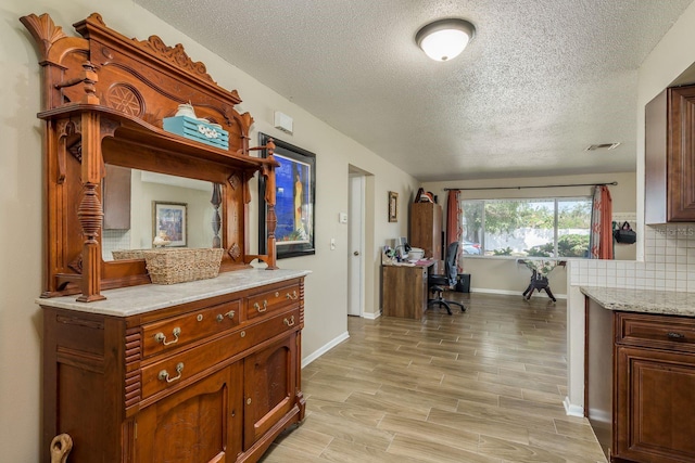 interior space featuring light wood finished floors, backsplash, a textured ceiling, light stone countertops, and baseboards