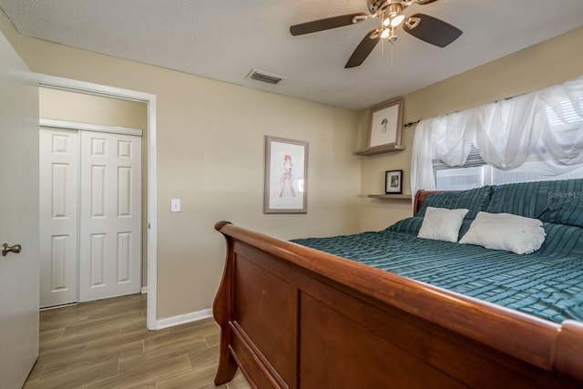 bedroom with a textured ceiling, wood finish floors, a ceiling fan, visible vents, and baseboards