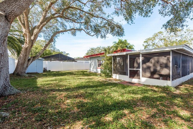 view of yard with a storage shed, an outbuilding, fence, and a sunroom