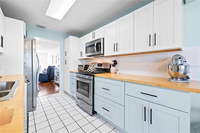 kitchen featuring wooden counters, decorative backsplash, stainless steel appliances, white cabinetry, and light tile patterned flooring