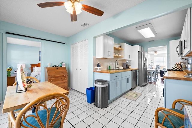 kitchen featuring stainless steel appliances, sink, light tile patterned floors, white cabinets, and butcher block countertops