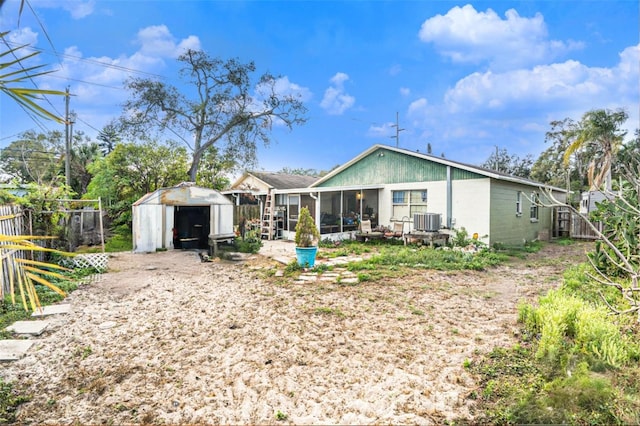 back of property featuring central air condition unit, a sunroom, and a shed