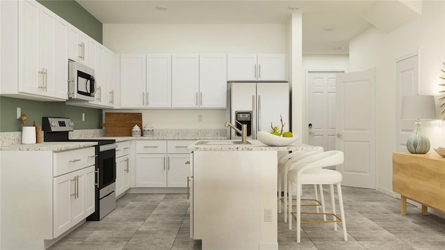 kitchen with sink, a center island, a kitchen bar, white cabinets, and appliances with stainless steel finishes