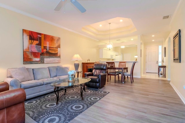 living room with ornamental molding, a tray ceiling, ceiling fan, a fireplace, and hardwood / wood-style floors