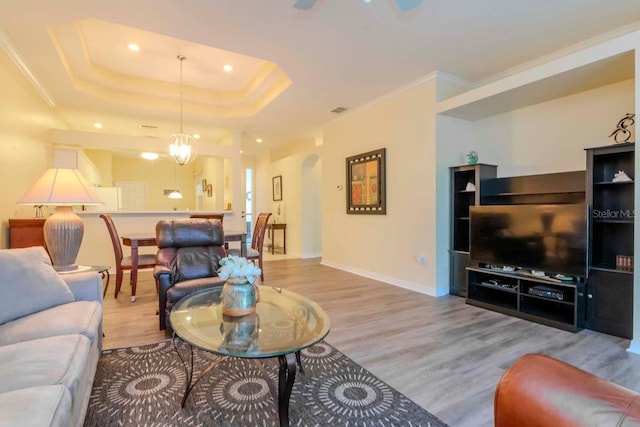 living room with a tray ceiling, ornamental molding, a notable chandelier, and light wood-type flooring