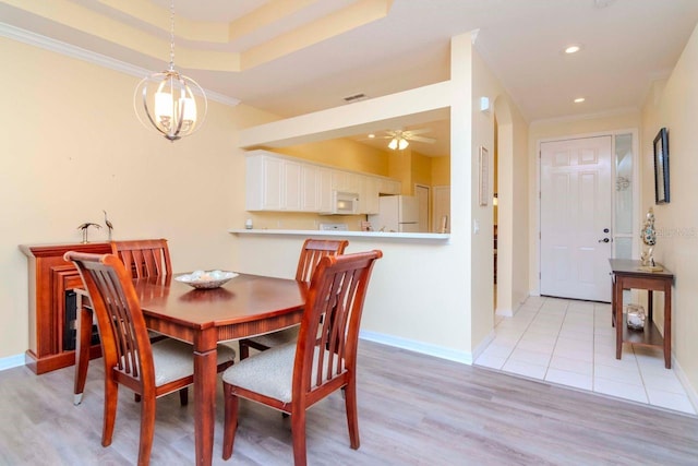 dining space with ceiling fan, a raised ceiling, ornamental molding, and light wood-type flooring