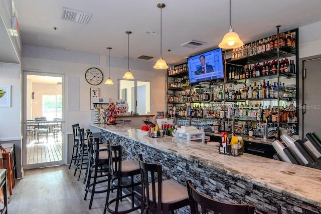 bar with hardwood / wood-style flooring, light stone counters, and hanging light fixtures