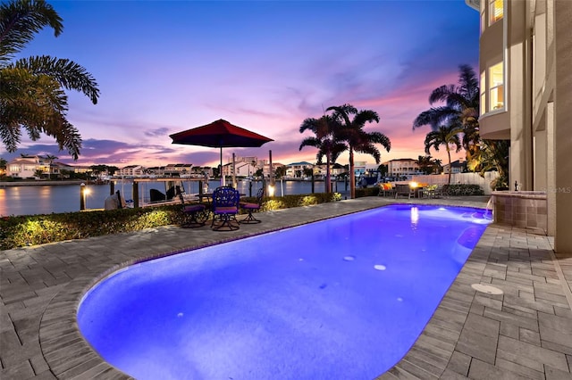 pool at dusk with a water view and a patio