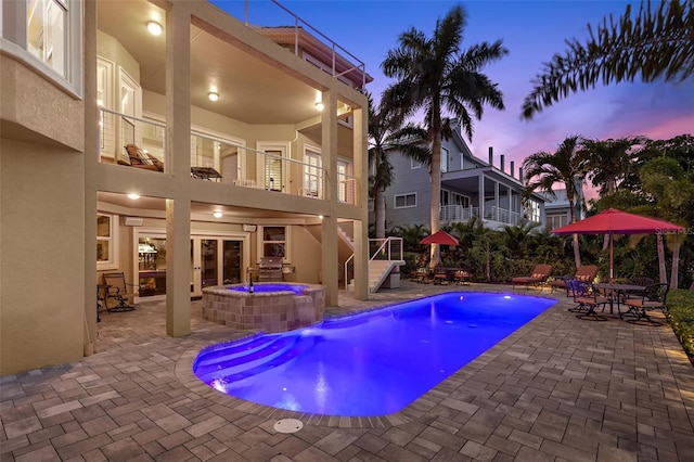 pool at dusk featuring a patio and an in ground hot tub