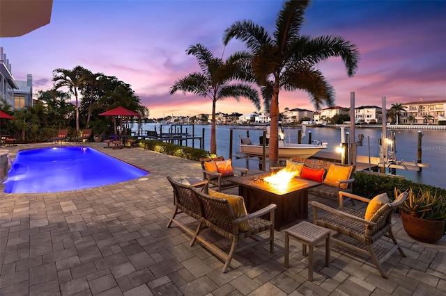 pool at dusk featuring an outdoor fire pit, a water view, a patio, and a dock