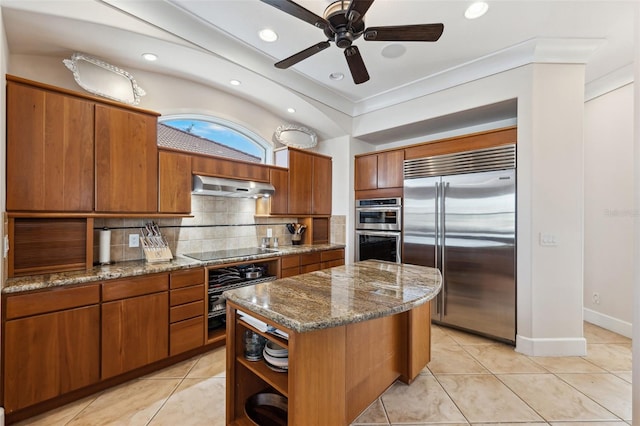 kitchen with appliances with stainless steel finishes, extractor fan, backsplash, a kitchen island, and dark stone countertops