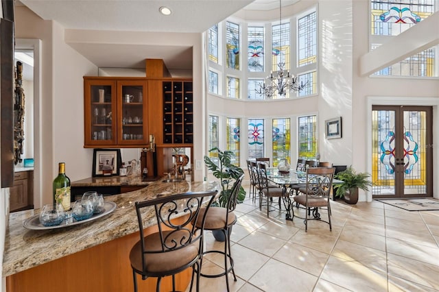 bar featuring french doors, an inviting chandelier, light stone counters, and light tile patterned floors