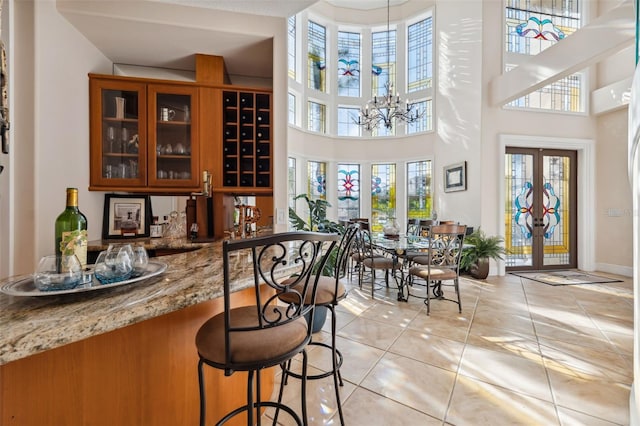 bar featuring a notable chandelier, light stone counters, french doors, a towering ceiling, and light tile patterned floors