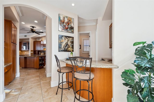 kitchen featuring kitchen peninsula, light stone countertops, light tile patterned flooring, tasteful backsplash, and a breakfast bar area