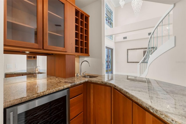 6015 Kipps Colony Dr E, Gulfport, FL 33707 - kitchen with wine cooler, brown cabinetry, light stone counters, and glass insert cabinets