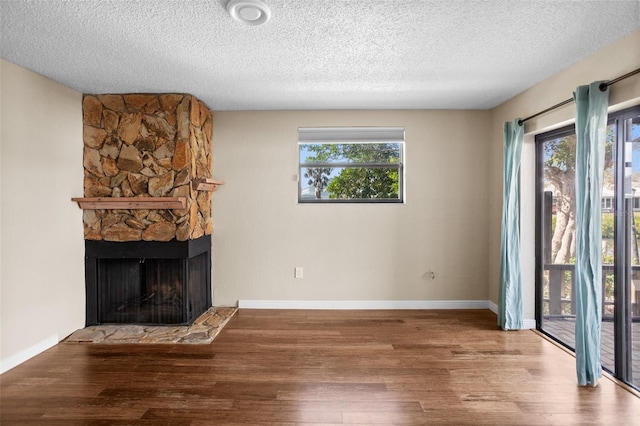 unfurnished living room with hardwood / wood-style flooring, a stone fireplace, plenty of natural light, and a textured ceiling