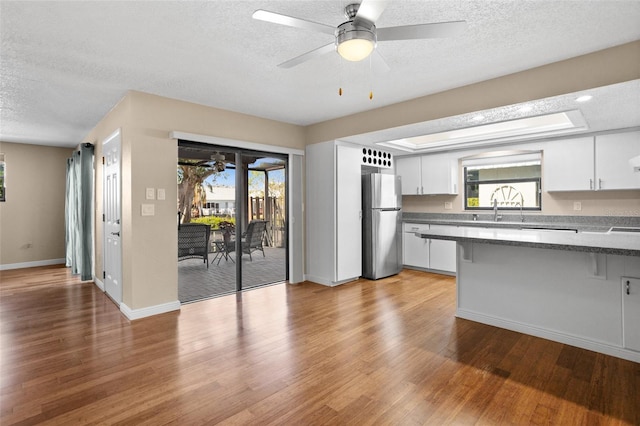 kitchen with white cabinetry, light wood-type flooring, stainless steel fridge, and ceiling fan