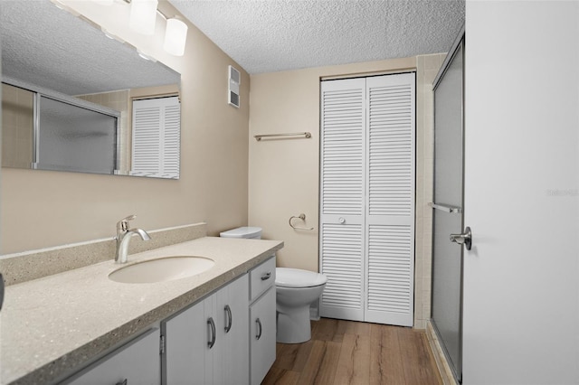 bathroom featuring toilet, a textured ceiling, vanity, a shower with door, and hardwood / wood-style floors