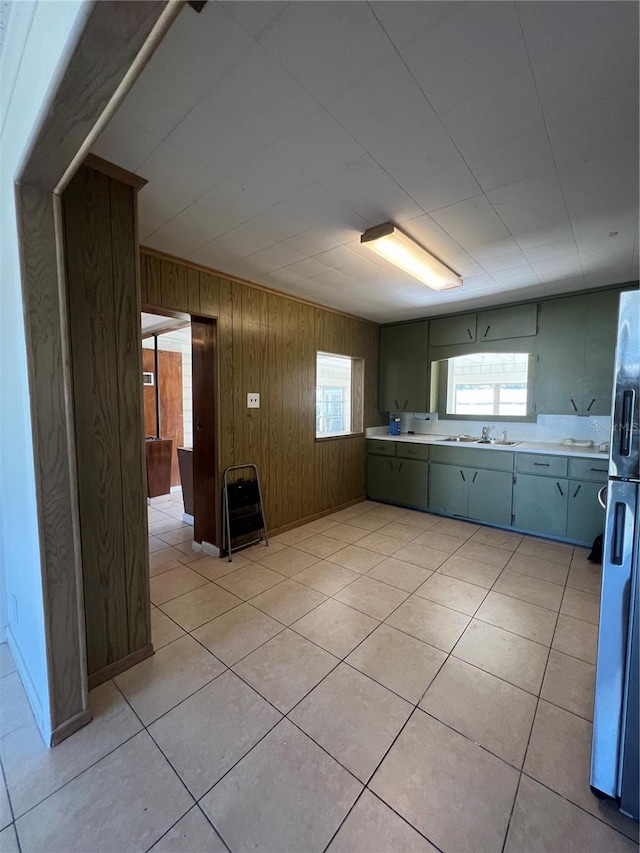 kitchen with stainless steel fridge, sink, light tile patterned floors, and wood walls