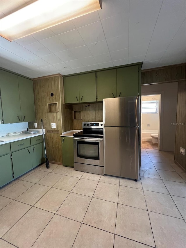 kitchen featuring wood walls, light tile patterned floors, stainless steel appliances, and green cabinetry