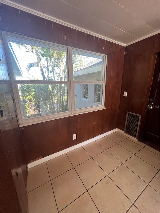 tiled empty room featuring crown molding, wooden walls, and a healthy amount of sunlight