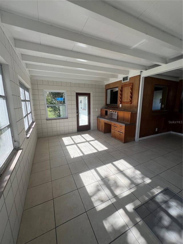 unfurnished living room with beamed ceiling, tile walls, and light tile patterned flooring