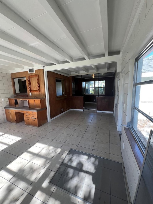 unfurnished living room featuring beam ceiling, light tile patterned floors, tile walls, and a wealth of natural light