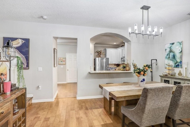 dining space with light hardwood / wood-style flooring, a textured ceiling, and an inviting chandelier